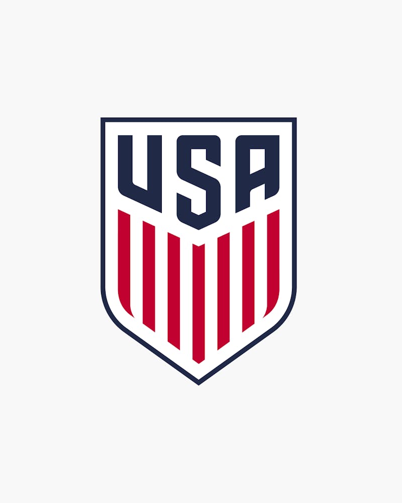 USA soccer logo featuring bold "USA" text above a shield with red vertical stripes on a white background.
