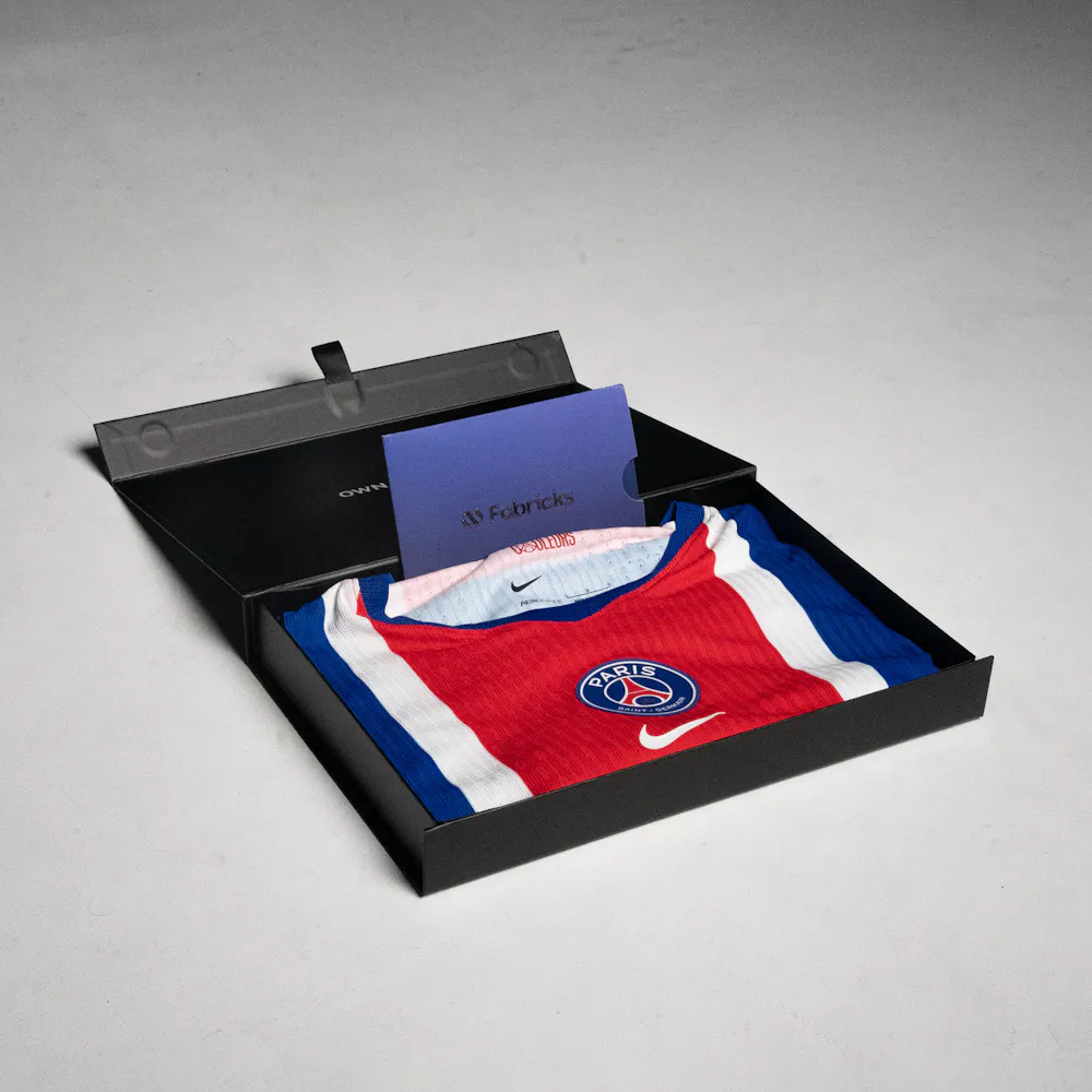 A red, white, and blue sports jersey with a club logo in an open black box, accompanied by a blue card labeled "Fabricks."